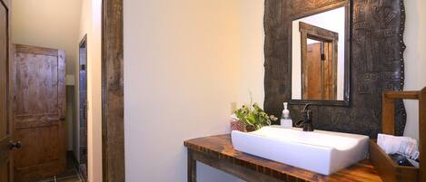 Un baño con tocador de madera, lavabo blanco, espejo con marco decorativo y perchero.