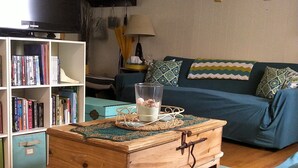 A living room with a wooden chest of drawers, a television, a bookshelf, and a blue sofa. - Cozy 2 Bedroom Cottage Walking Distance to the Beach (Zurich)