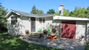 A single-story house with a garage, a front porch with steps, and a chimney. - Cozy 2 Bedroom Cottage Walking Distance to the Beach (Zurich)