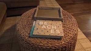Una habitación con un sofá marrón, un reposapiés de mimbre y un libro, y una puerta de madera.