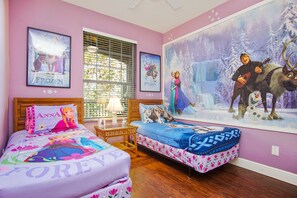 Quarto com duas camas, cada uma com roupa de cama temática, um grande mural na parede e uma janela com persianas.