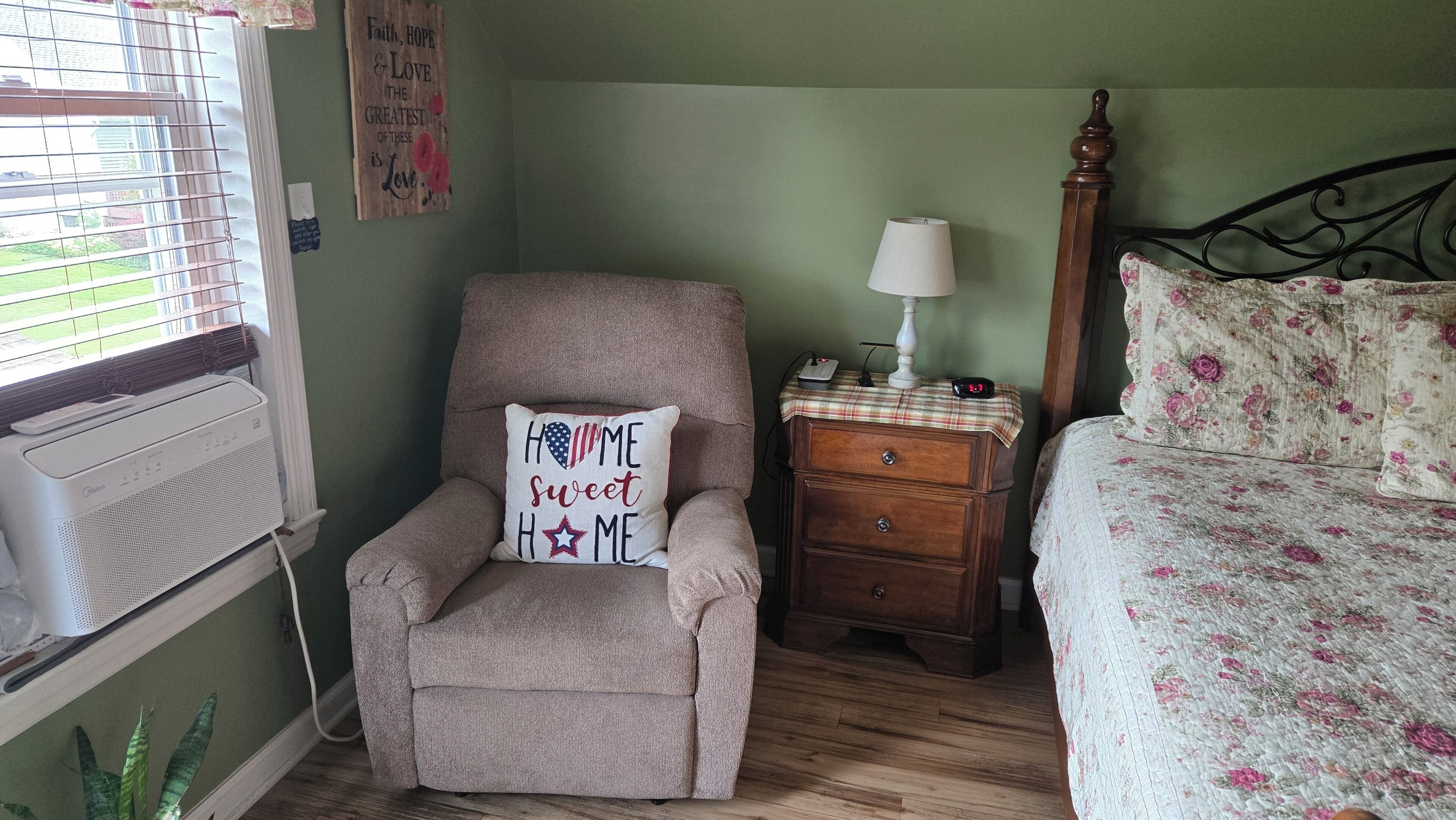 Een gezellige kamer met een fauteuil, een houten nachtkastje, een nachttafel met een lamp en een bloemenbedekt sprei.