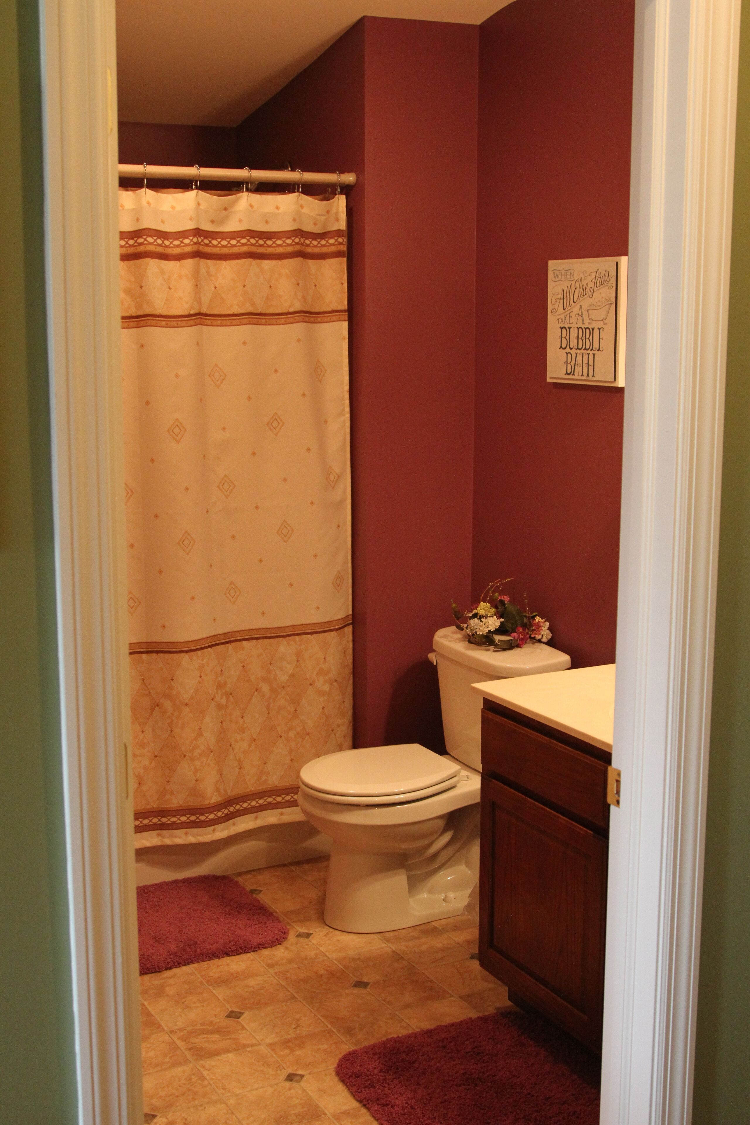 A bathroom with a toilet, a shower curtain, a wooden cabinet, and a sign on the wall.