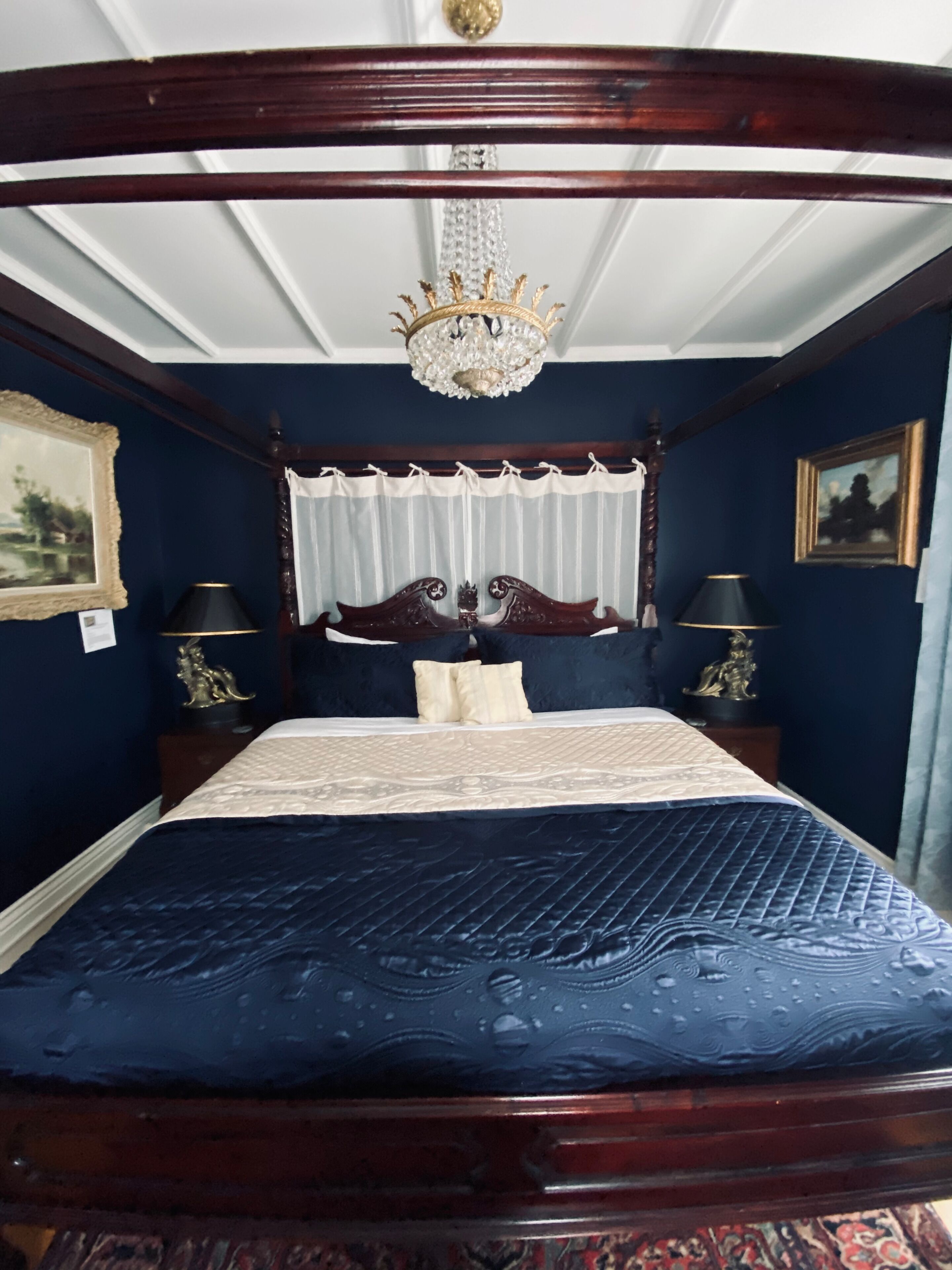Una cama con dosel y doselajes, con un edredón azul oscuro.