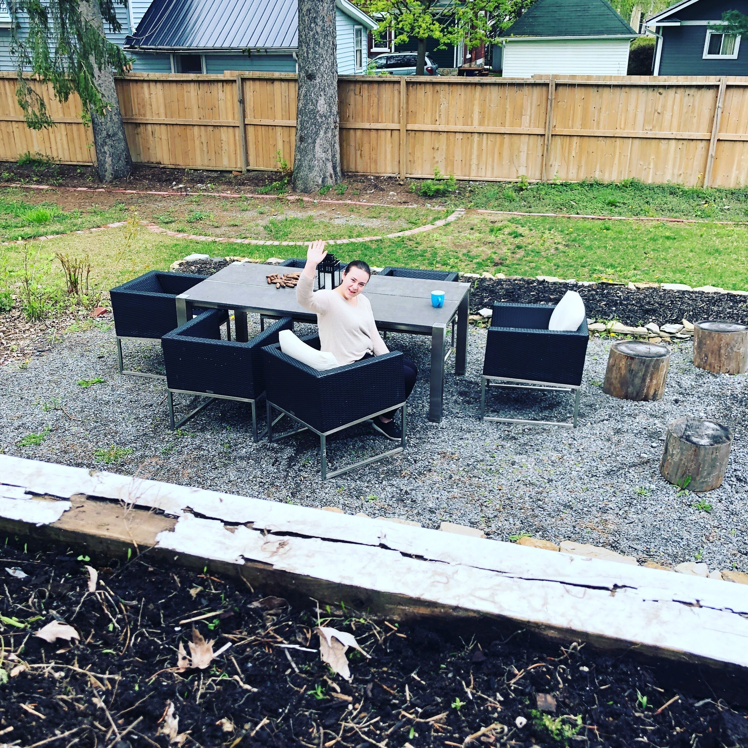 Une terrasse extérieure avec une table et des chaises, entourée d’une clôture en bois et d’un jardin.