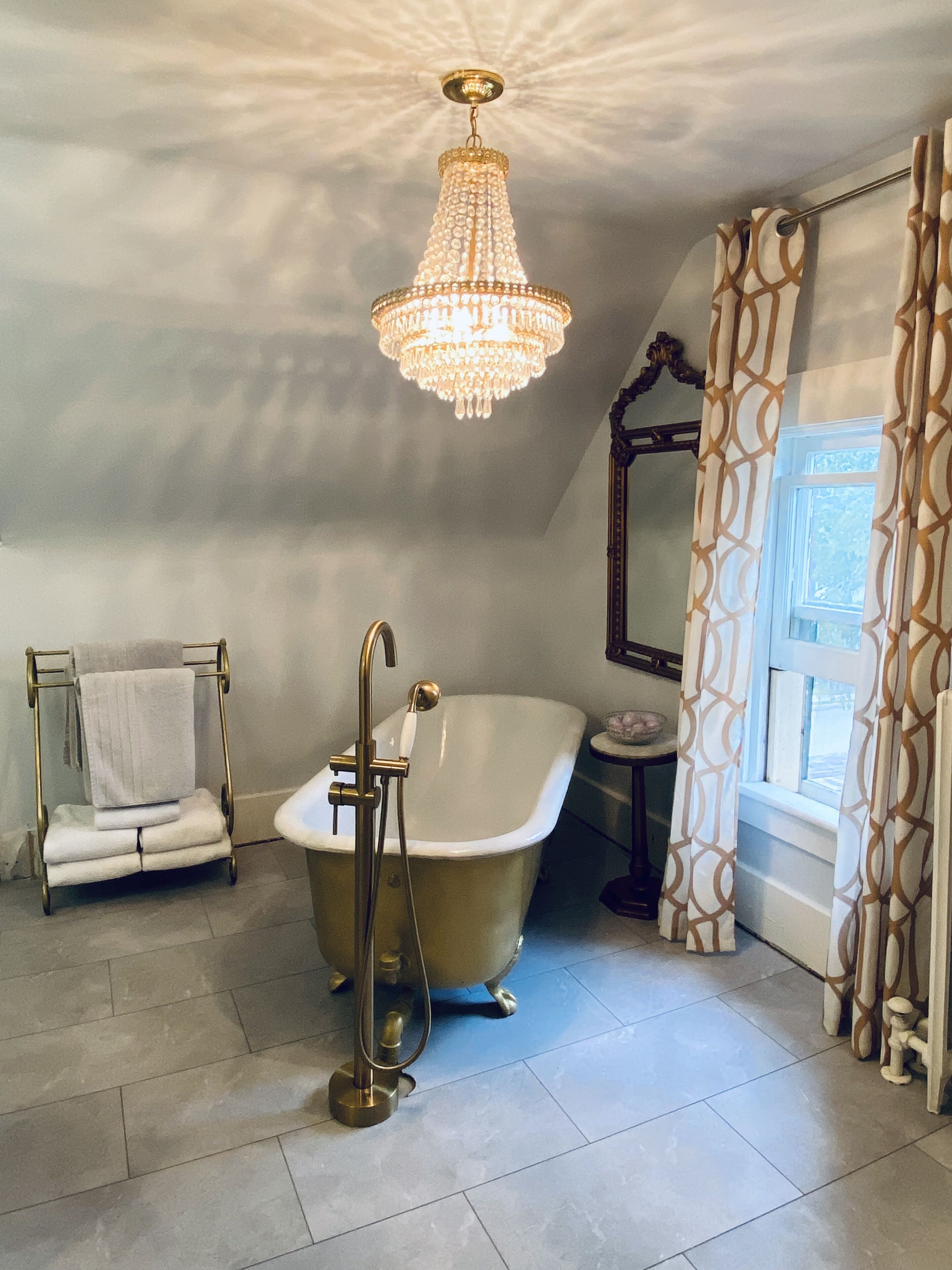 Une salle de bain avec une baignoire sur pieds, un porte-serviettes avec des serviettes pliées, une petite table avec un bol et un grand miroir.