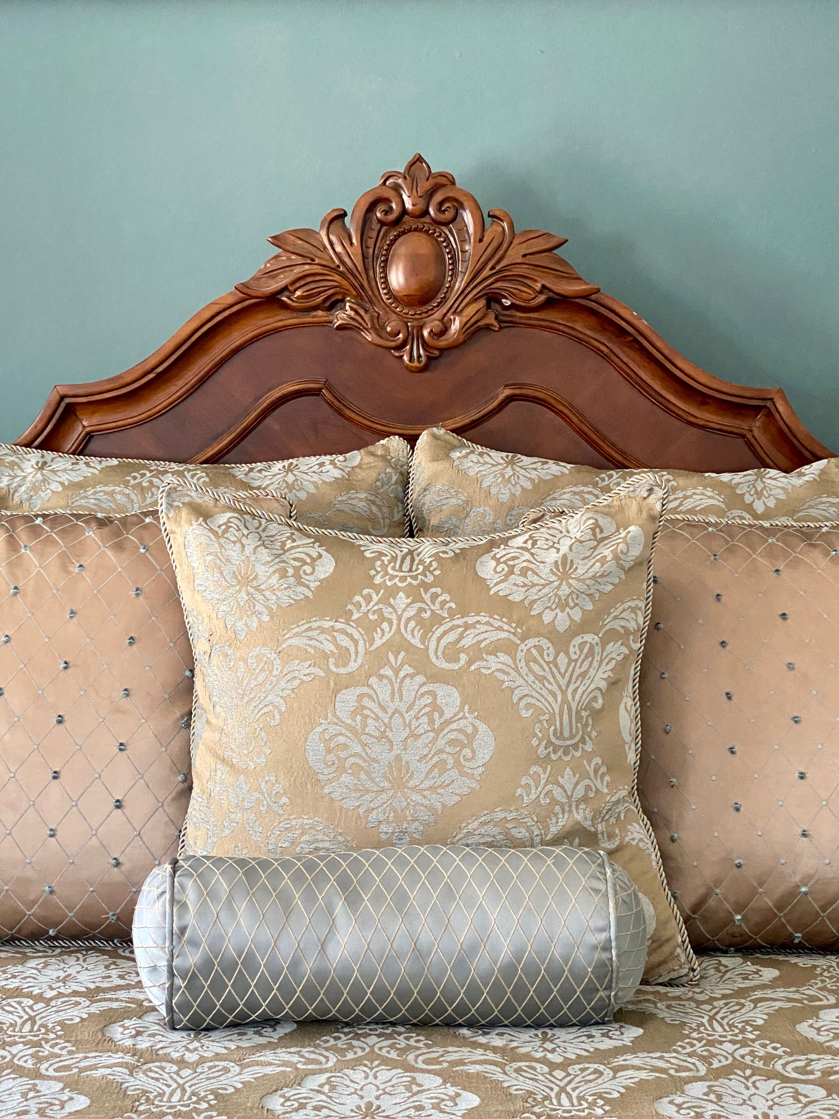Un lit avec une tête de lit en bois, des coussins à motifs et une couverture matelassée.