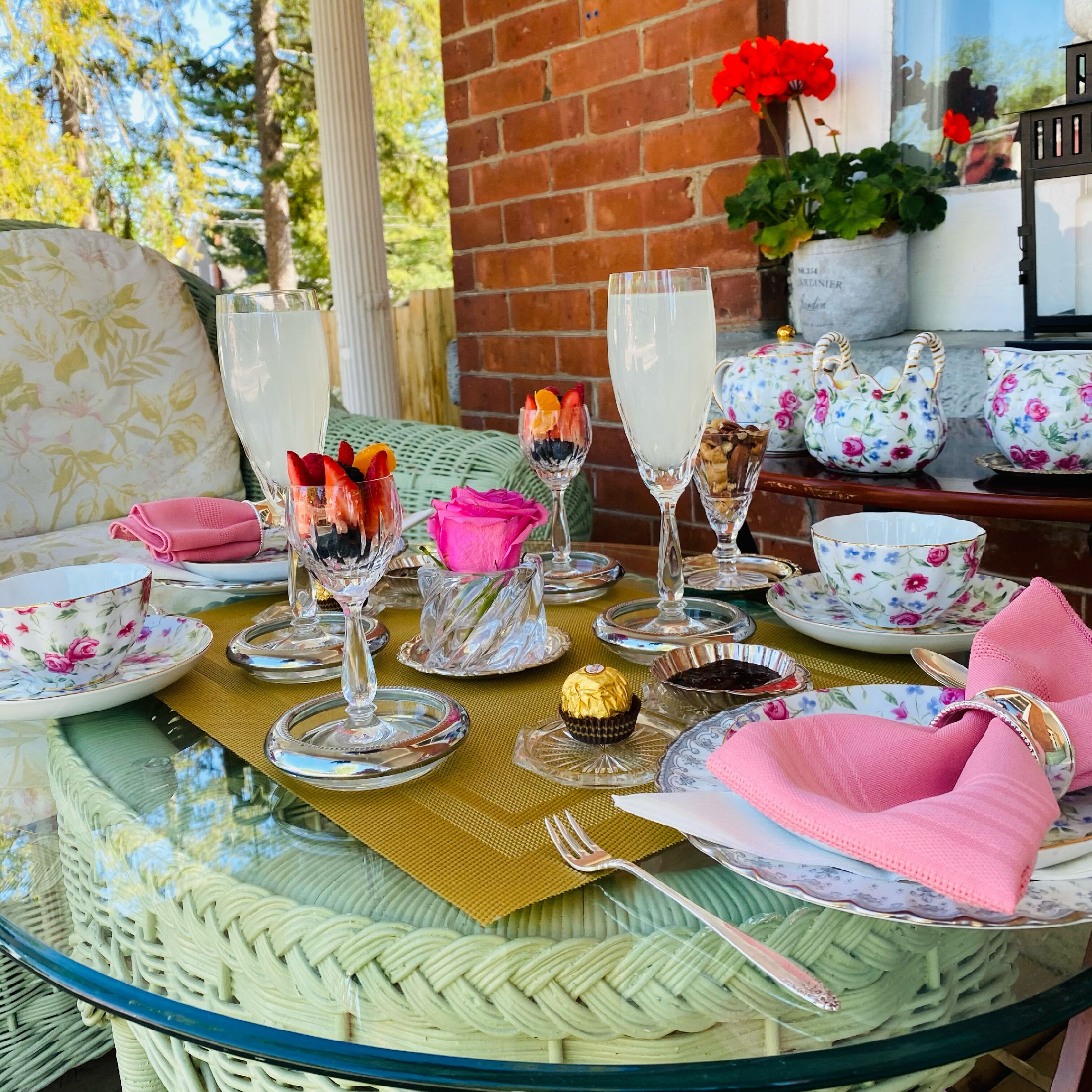 A round glass table set with floral-patterned plates, a pink napkin, and clear glassware.