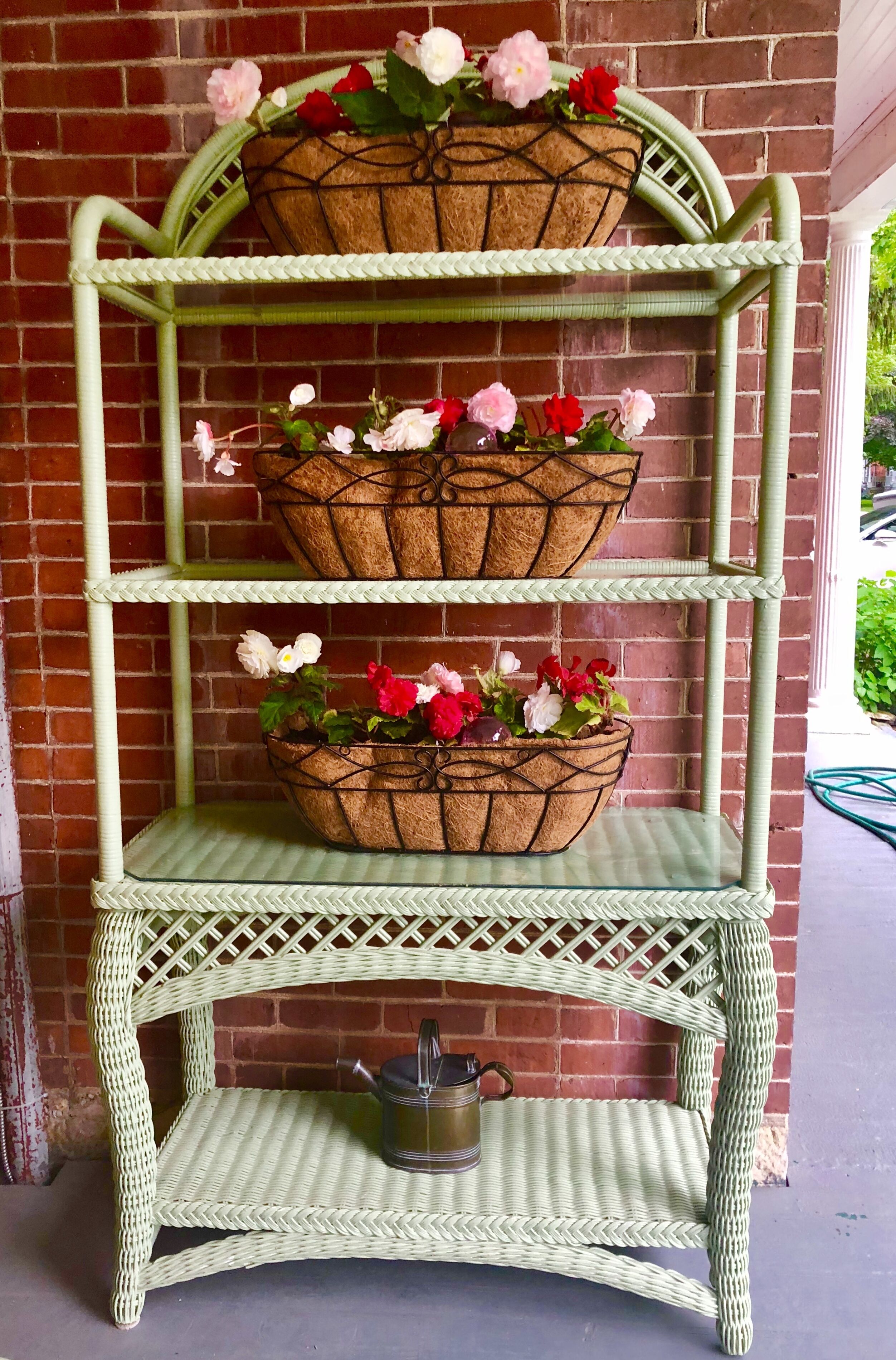 A green wicker shelf unit with three baskets containing flowers.