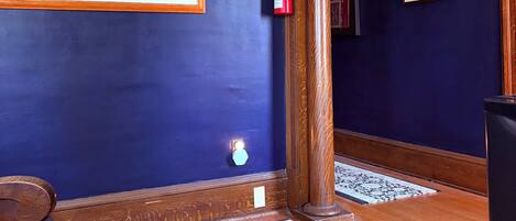 A hallway with dark blue walls, a framed historical sports illustration, a fire extinguisher, and a patterned rug.