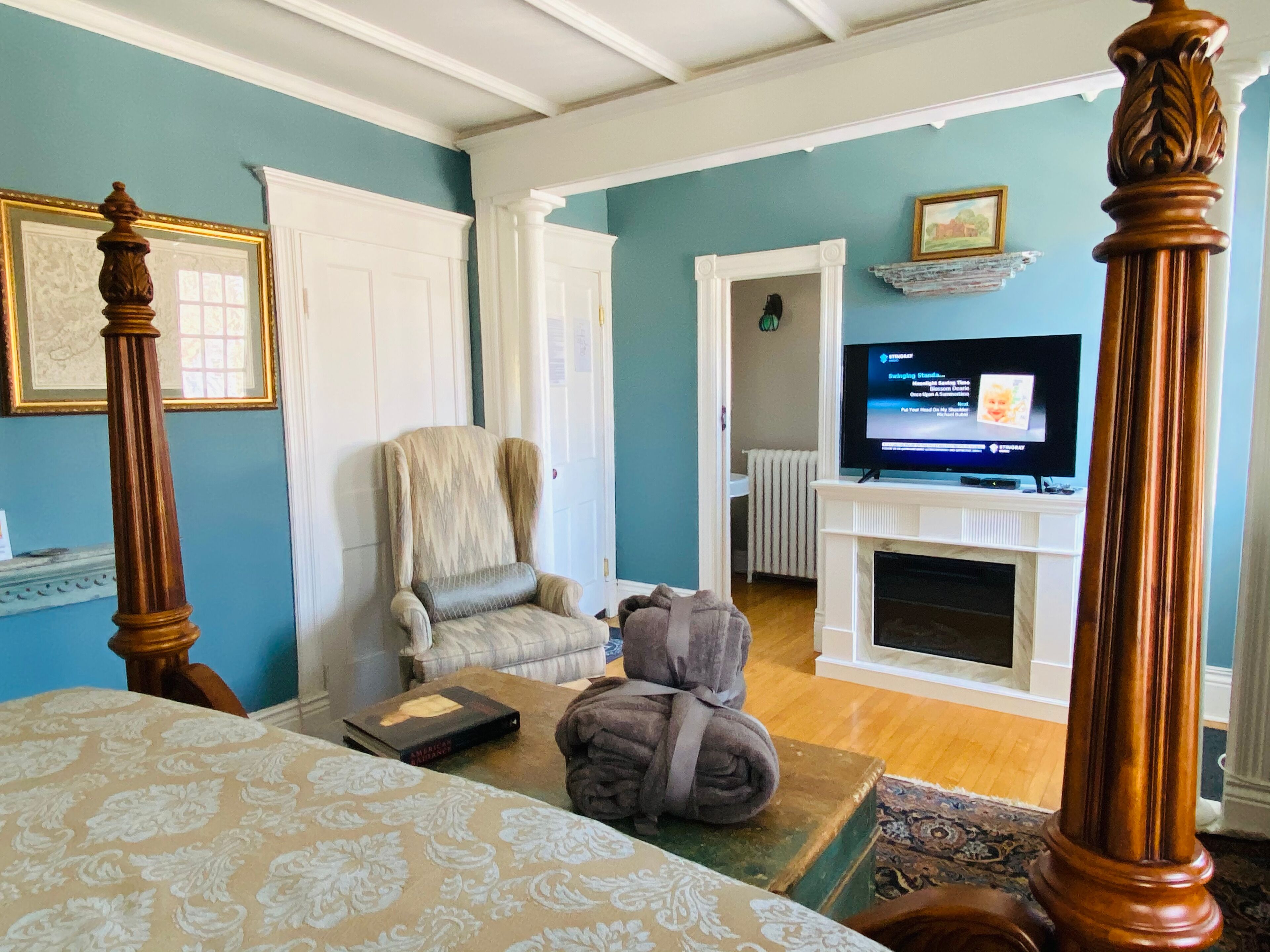 Un dormitorio con una cama con dosel, televisión, chimenea y una silla.