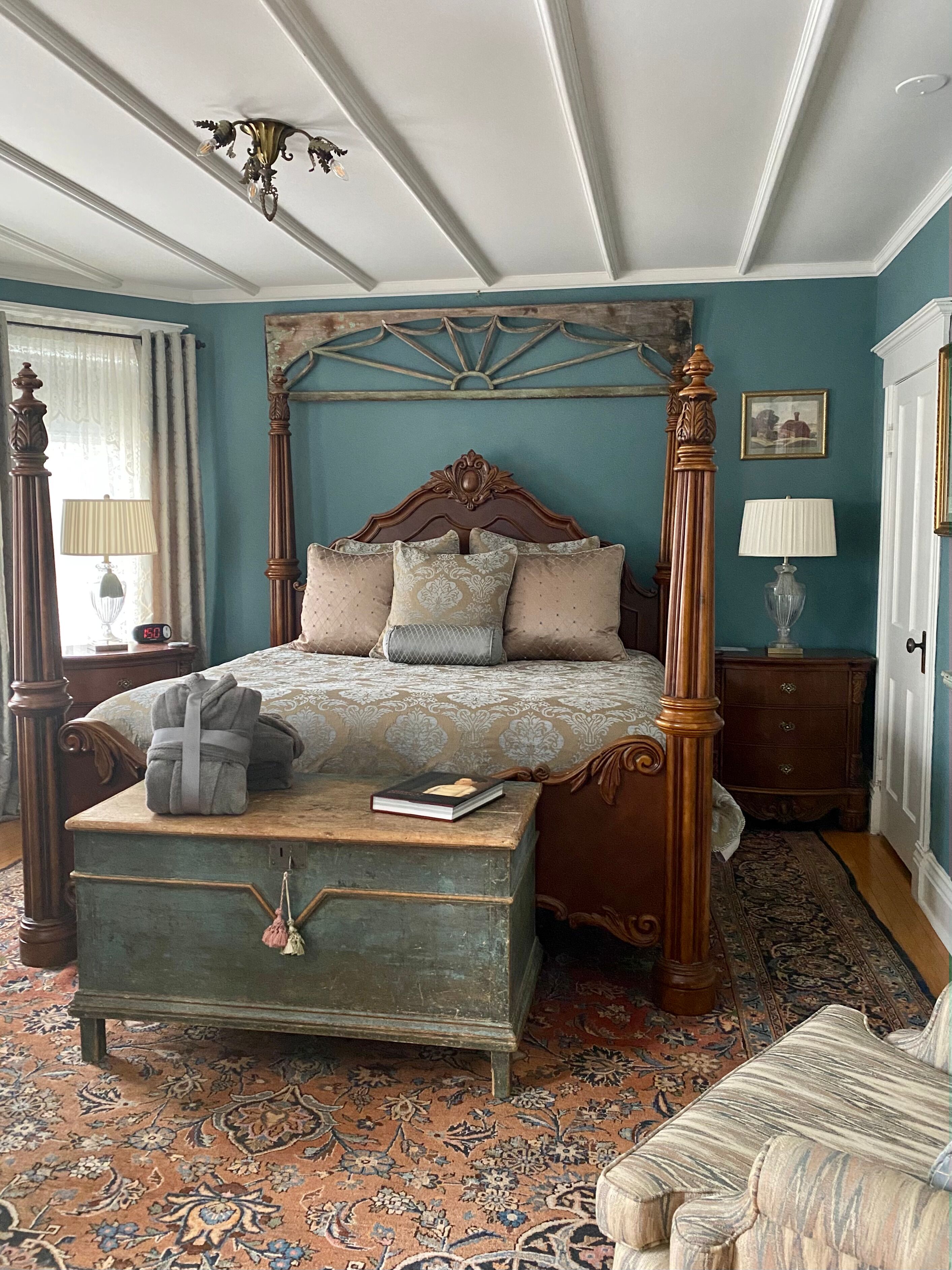 A four-poster bed with a wooden headboard, a bedside table, a nightstand, a bench, and a patterned rug.