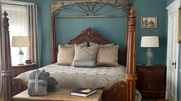 A four-poster bed with a wooden headboard, a bedside table, a nightstand, a bench, and a patterned rug.