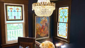 Una habitación con candelabro, dos sillones con cojines estampados, una mesa con un jarrón de flores y un cuadro en la pared.