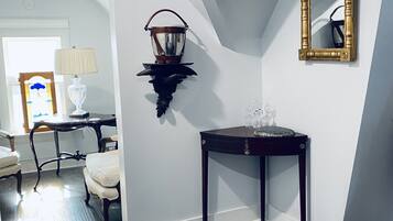 Una habitación con suelo de madera oscura, pared blanca, consola de madera oscura con superficie de vidrio, lámpara de pared y un espejo.
