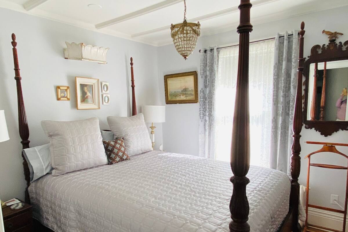 A four-poster bed with a white quilt, a chandelier, and a mirror with an ornate frame.
