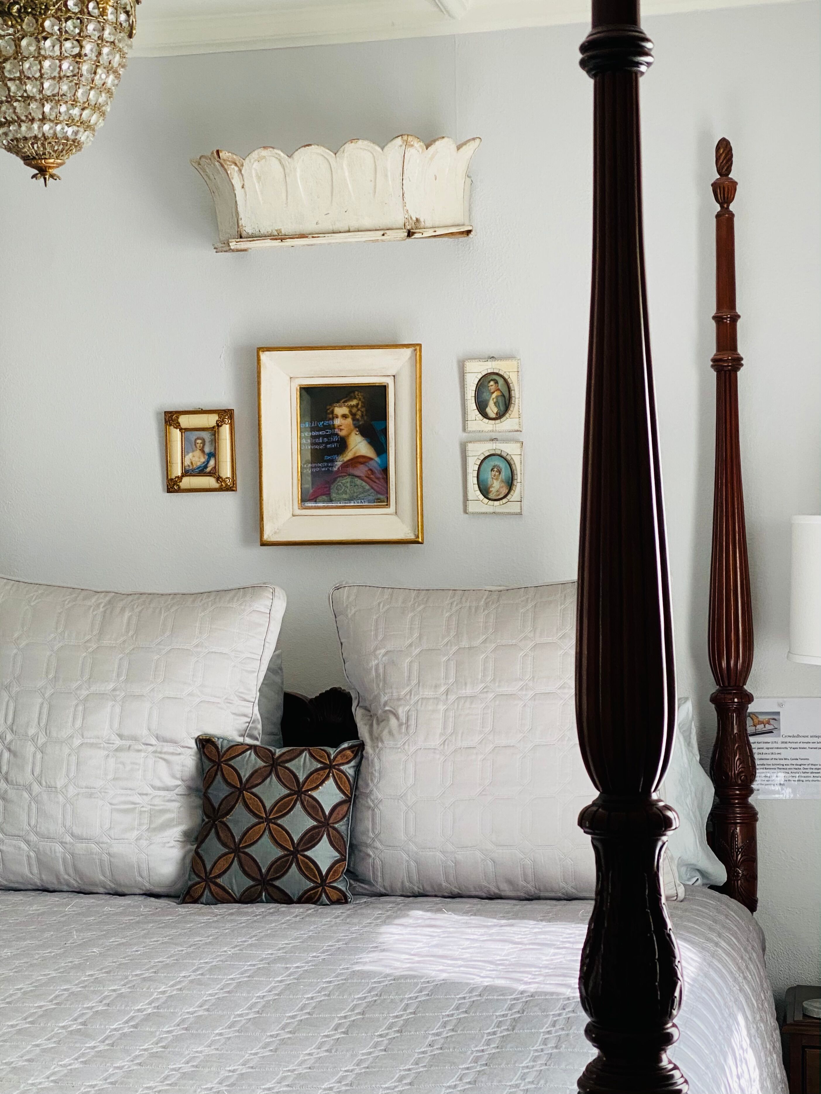 Ein Schlafzimmer mit Himmelbett, einer Chandelüster und gerahmten Kunstwerken an der Wand.