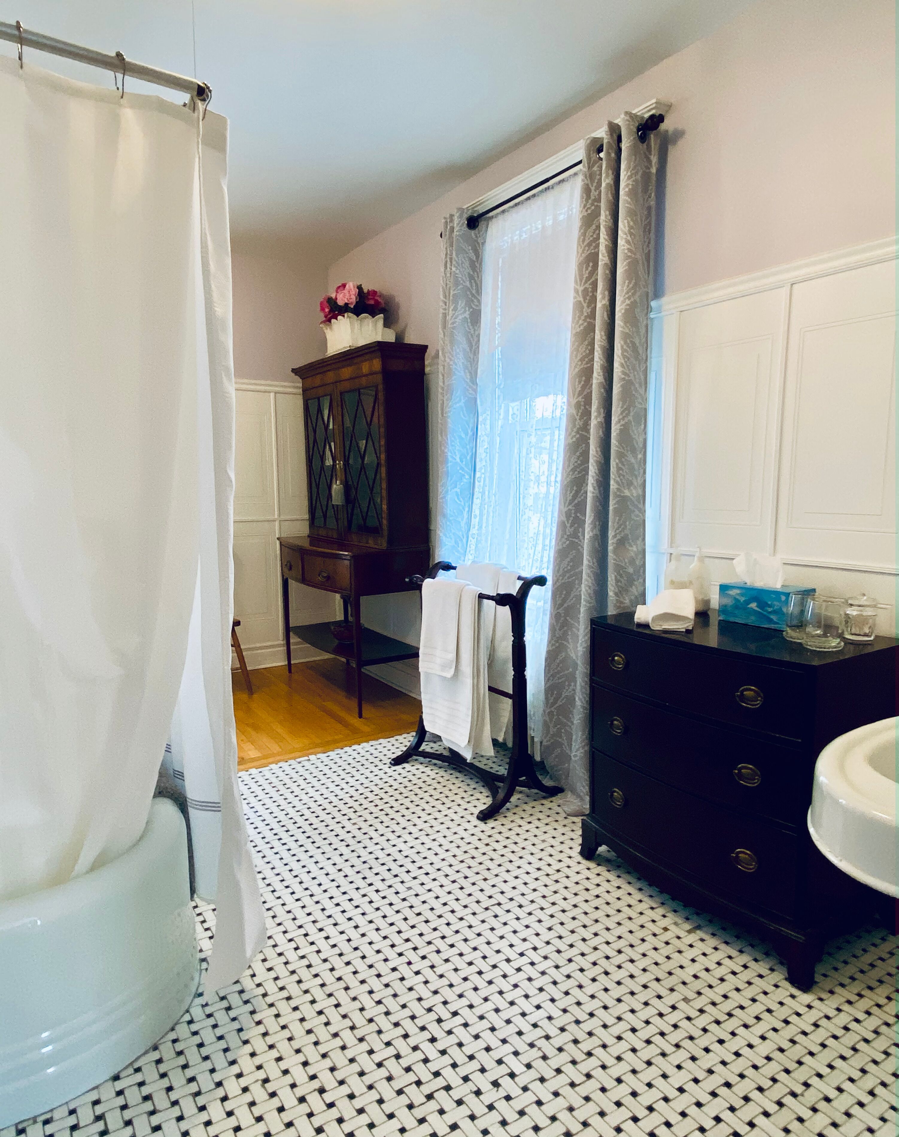 Un baño con inodoro blanco, un mueble de madera oscura, piso estampado y cortina de ducha.