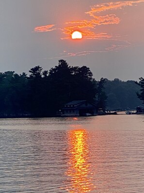 A sunset over a calm lake with a house on the shore. - 1000 Islands B&B – The Bulloch House (Gananoque)