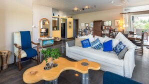 A modern living room with a white sofa, blue cushions, a wooden coffee table, and a dining area with a table and chairs. - Lagonisi Villa Afroditi (Saronikos)