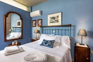 A bedroom with a bed, a mirror, framed pictures, and a nightstand with a lamp. - Lagonisi Villa Afroditi (Saronikos)