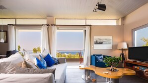A modern hotel room with a large bed, a sofa, a curved wooden coffee table, a TV, and a view of the sea. - Lagonisi Villa Afroditi (Saronikos)