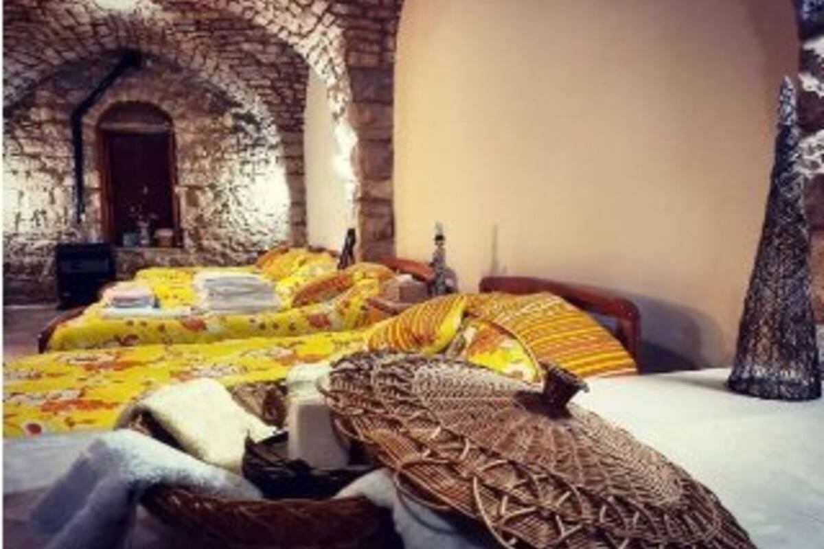 Ein Zimmer mit einem steinernen Bogen, einem Bett mit gelber Bettdecke und einem gewebten Korb.