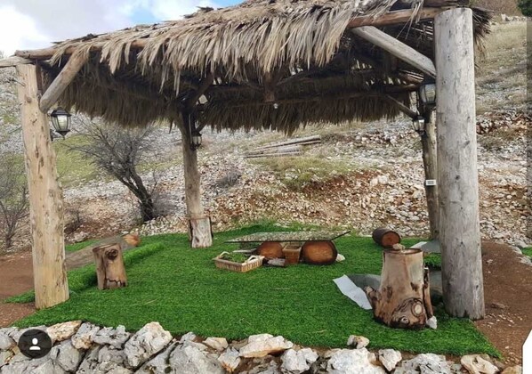 A rustic wooden structure with a thatched roof, surrounded by a green lawn and stone walls.