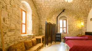 Habitació amb parets de pedra, un sofà de fusta, dos llits amb roba de llit vermella i una taula petita.