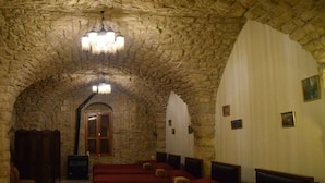 Habitació amb parets de pedra, una catifa vermella, un penjador i una taula de fusta amb un ram i un llibre.