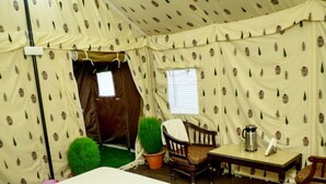 A tent with a patterned fabric interior, a wooden chair, a small table with a kettle, and a potted plant. - Kumbha Kamps (Prayagraj)