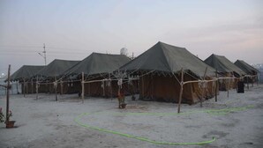 A row of tents with a sandy ground, some potted plants, and a green hose. - Kumbha Kamps (Prayagraj)