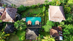 An aerial view of a resort with a central swimming pool, surrounded by lush greenery and multiple bungalow-style buildings with sloped roofs. - Villa Manuk (Sawan)