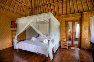Una habitación con una cama bajo un dosel, pisos de madera y un muro tejido.