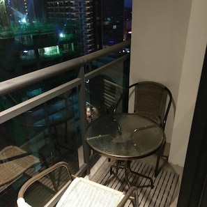 Ein Balkon mit Glastisch und Stühlen, der auf eine beleuchtete Stadtlandschaft blickt.