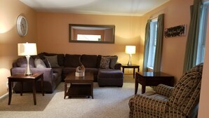 A living room with a sectional sofa, a coffee table, two side tables with lamps, a patterned armchair, a clock on the wall, and a framed picture. - Your Home away from Home. Large Groups Welcome (Hamden)