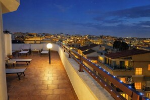 A rooftop terrace with outdoor seating and a view of a cityscape at dusk.