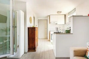 A narrow hallway leading to a kitchen with white cabinets, a wooden cabinet, and a door at the end.