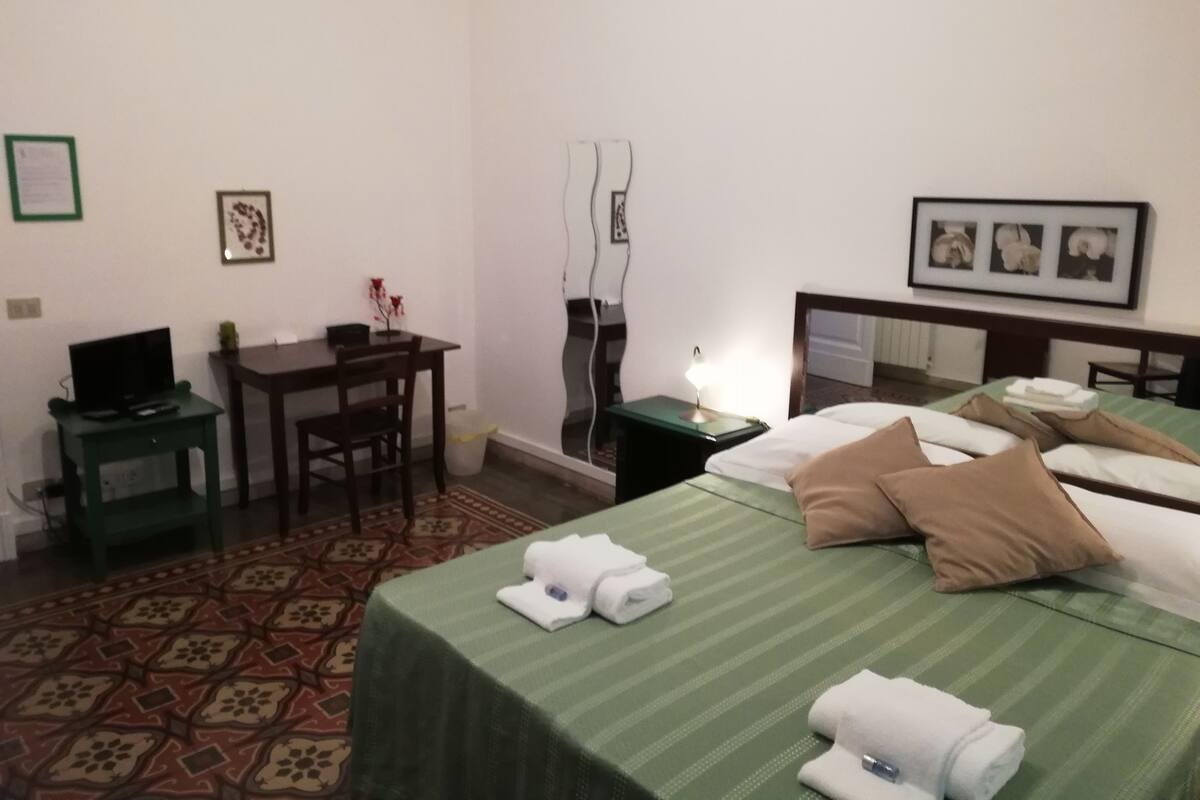 A hotel room with two beds, a desk, a chair, a TV, and a small table.