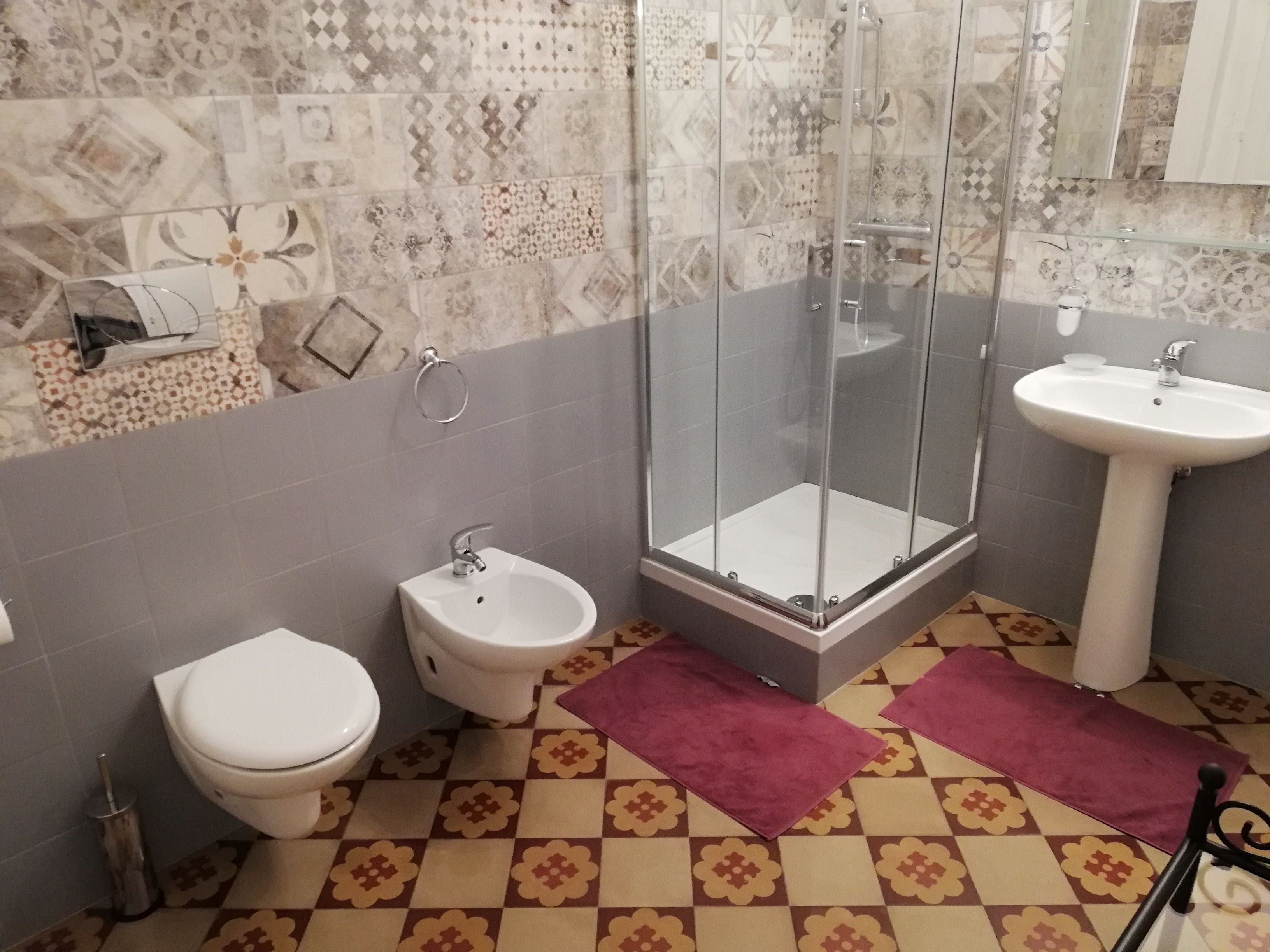 A bathroom with a toilet, bidet, glass-enclosed shower, and a sink.