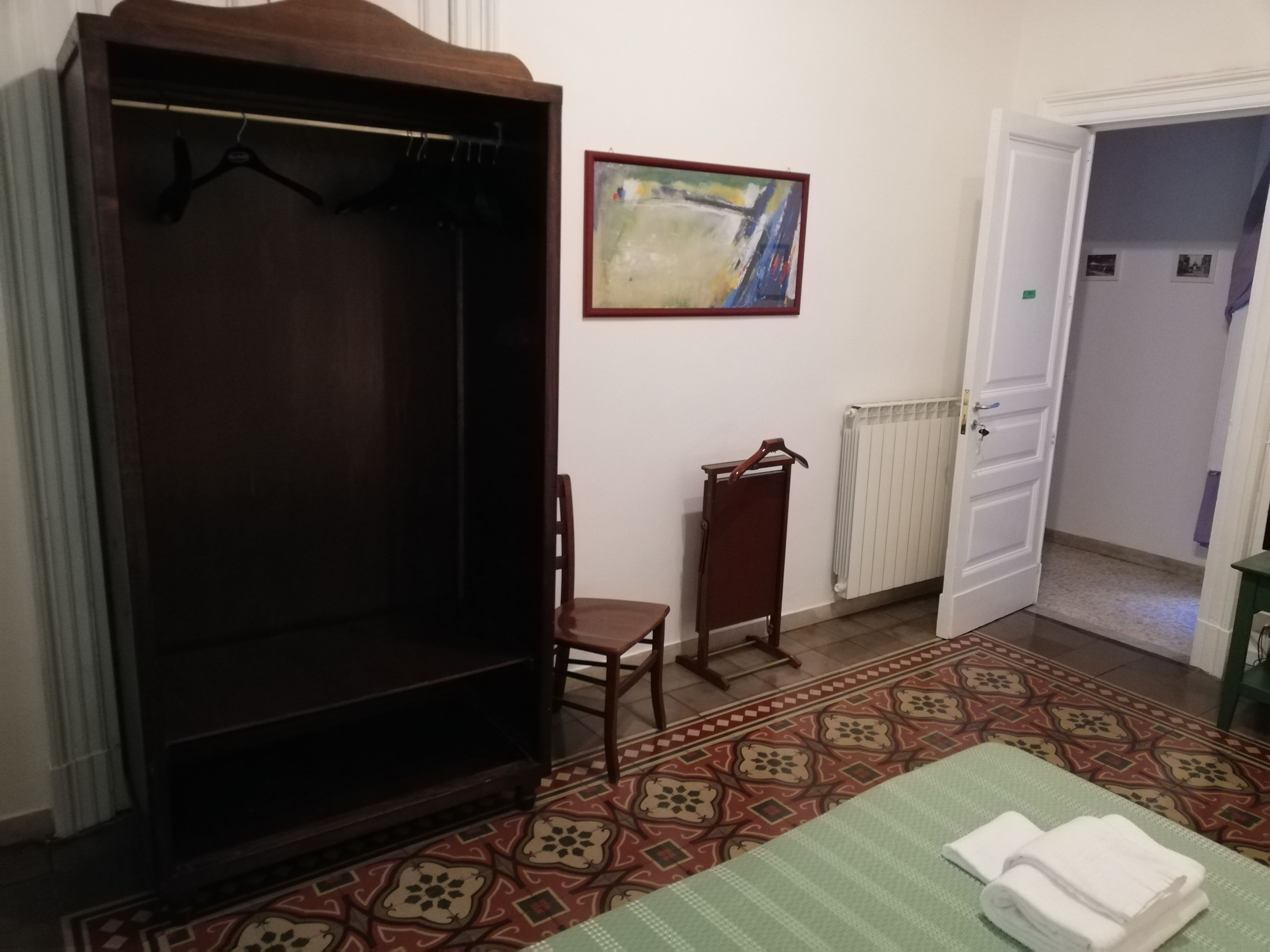 Une pièce comprenant une armoire, une chaise, un radiateur, un tapis à motifs et un tableau accroché au mur.