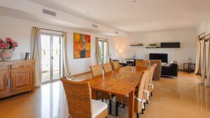 Uma sala de estar ampla com uma grande mesa de jantar, assentos confortáveis, lareira e televisão.