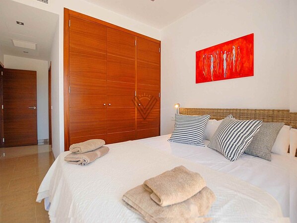 Quarto com um guarda-roupa de madeira grande, uma cama com várias almofadas e um quadro abstrato vermelho na parede.