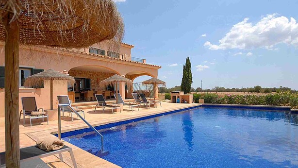 Área de piscina com espreguiçadeiras, um guarda-sol de palha e vista para o campo.