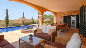 Uma área externa coberta com piscina, espreguiçadeiras, mesa de jantar e parede de pedra.