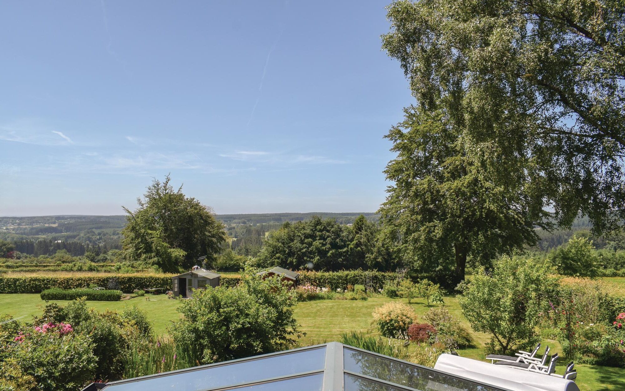 Un jardin avec un petit abri de jardin, une pelouse et un grand arbre.