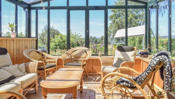 Un invernadero con muebles de mimbre, una mesa de madera y vistas al follaje.