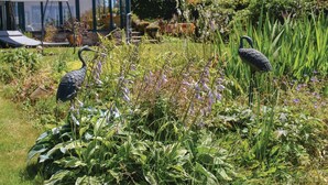 Un jardín con dos esculturas de aves, un invernadero y una variedad de plantas.