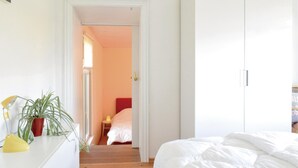Un dormitorio con cama, armario, mesita de noche con lámpara y una planta en maceta.