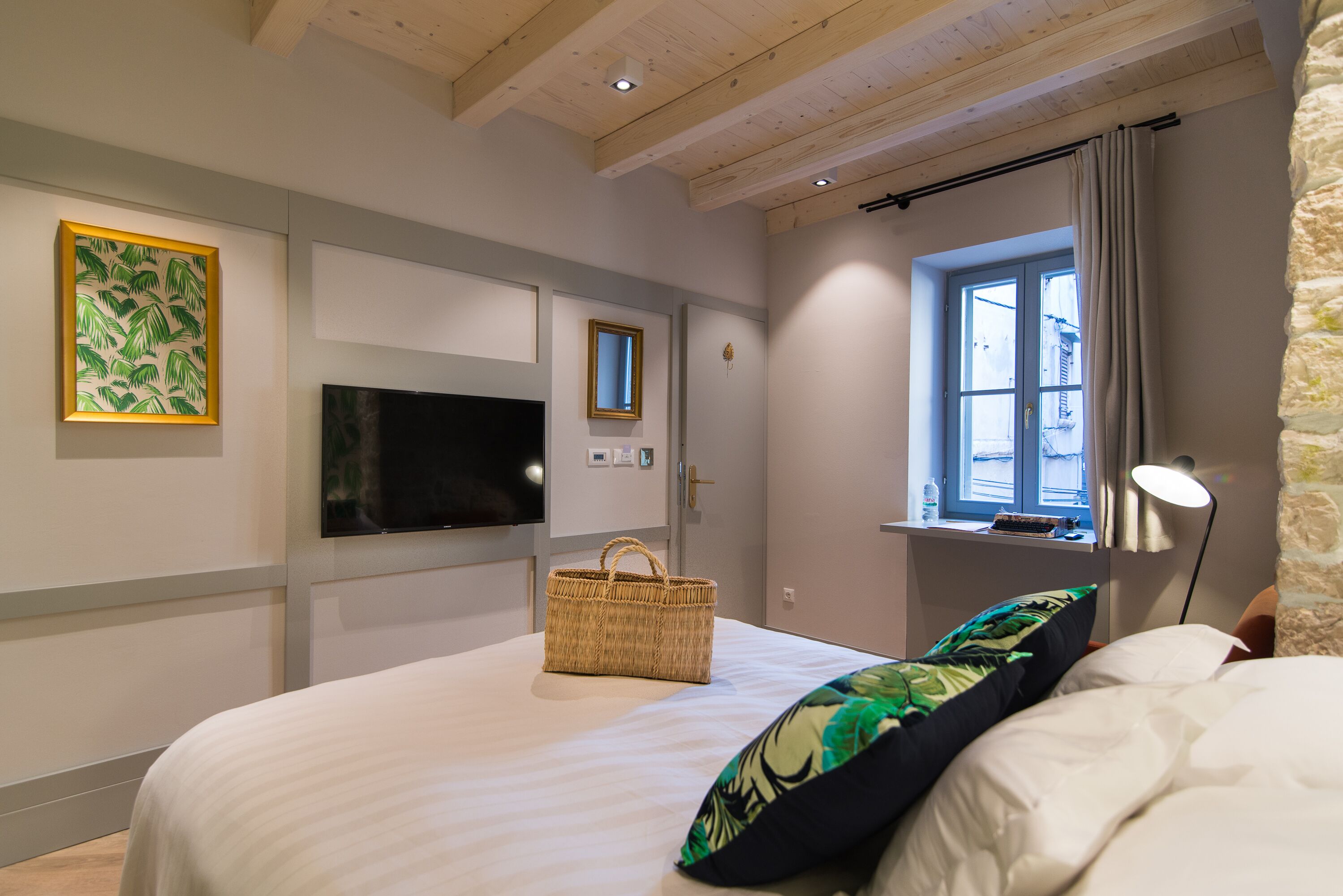 A bedroom with a bed, a TV, a window, and a basket on the bed.